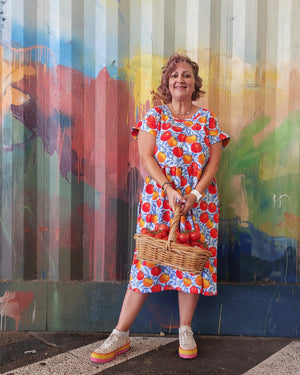 Woman in a colorful dress holding a basket in front of a mural.