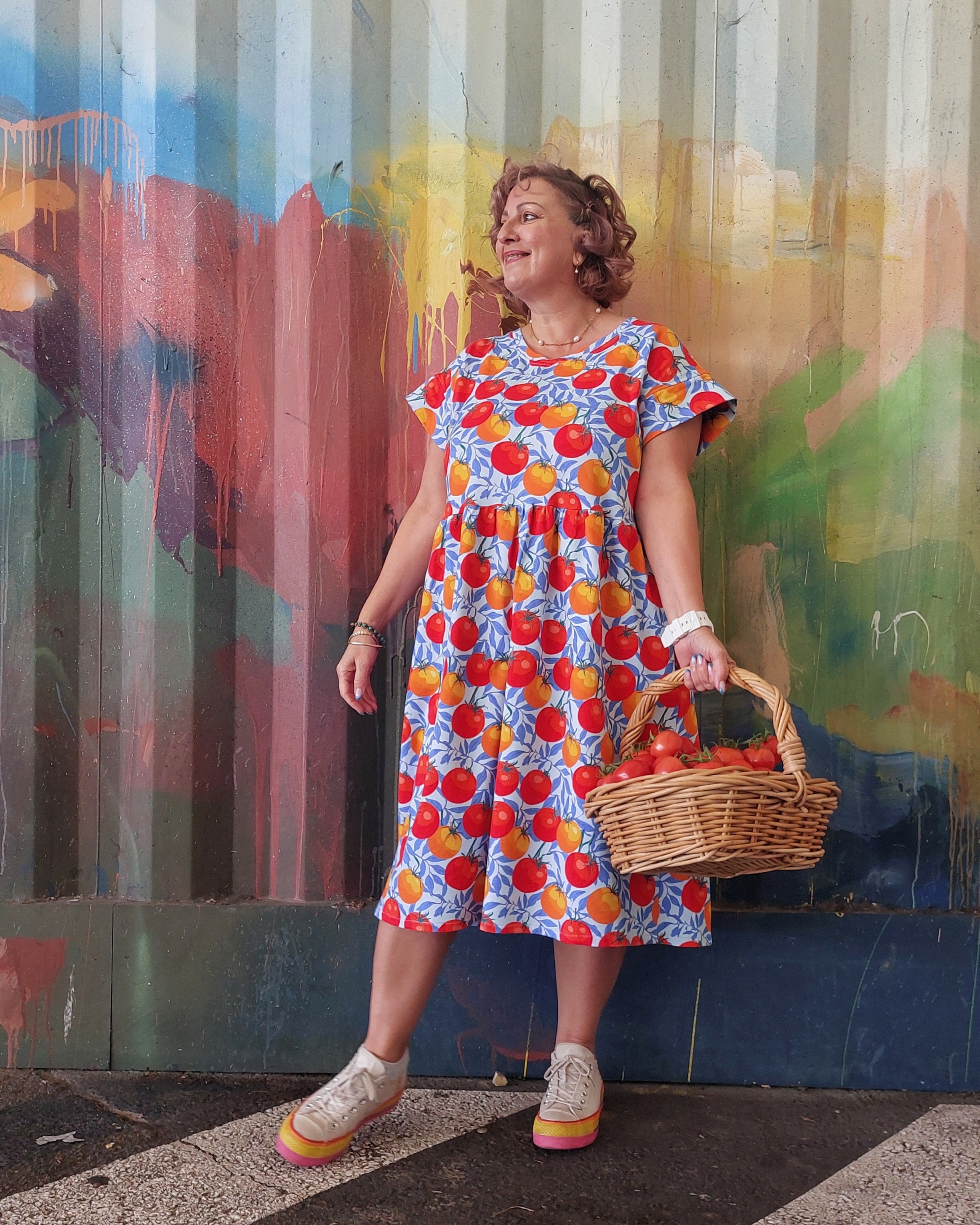 Woman in a colorful dress with fruit pattern standing against a graffiti wall.