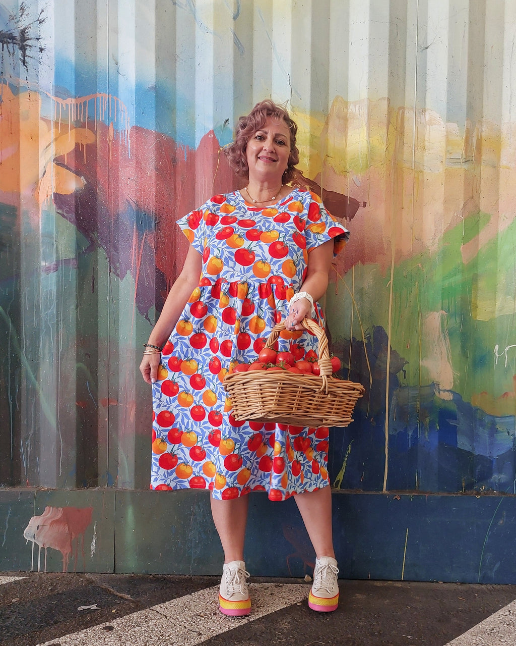 Woman in a colorful dress holding a basket against a vibrant mural.