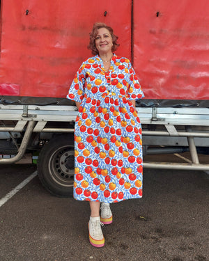 Woman wearing a colorful dress with fruit pattern standing in front of a red truck.